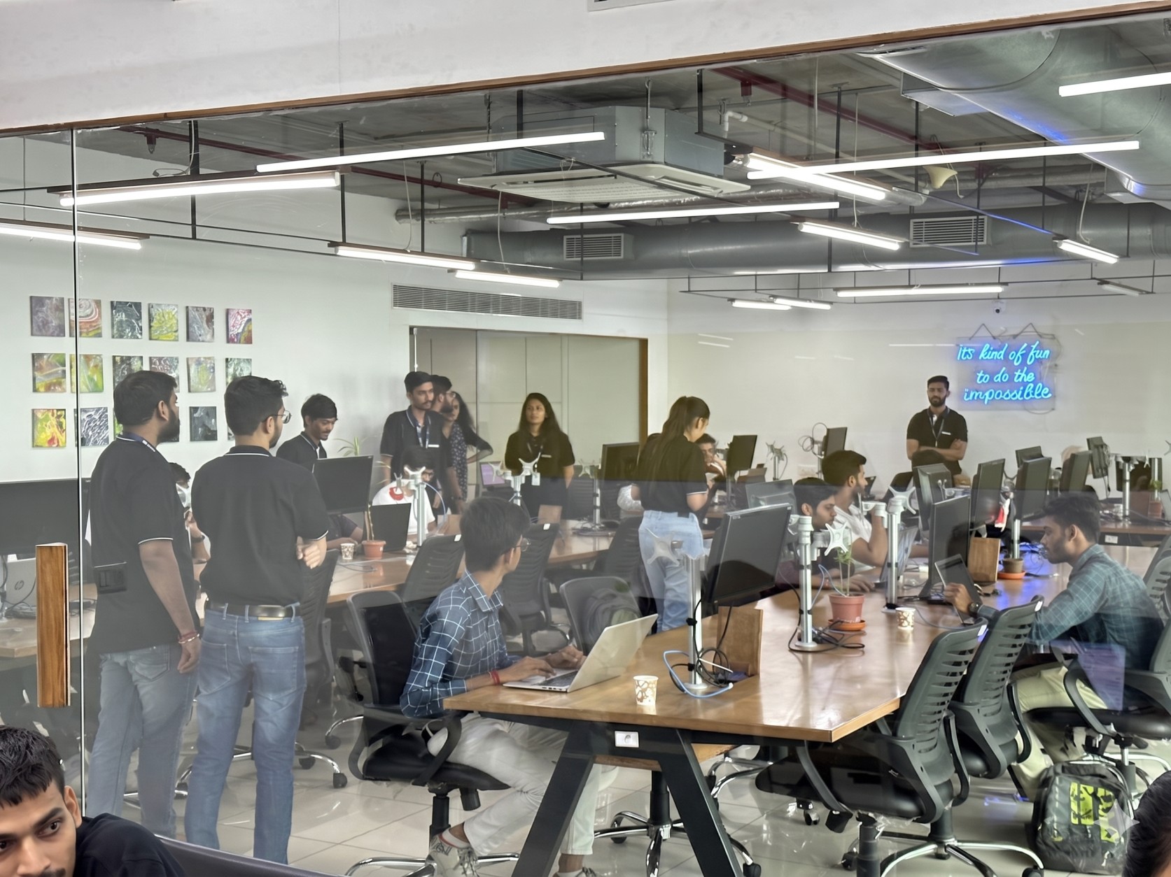 Web Mavens engineering team collaborating in our open-plan office, with team members standing and working at desks under a neon sign that reads 'It's kind of fun to do the impossible'